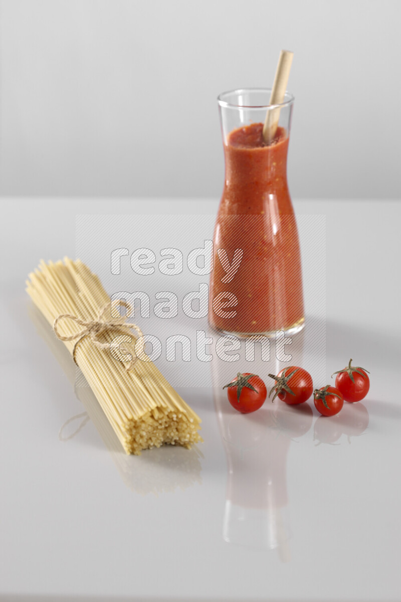 Raw pasta with tomatoe pasta with different ingredients such as cherry tomatoes, basil, garlic, bay laurel, cardamom, white pepper, black pepper, red chilis and wheat stalks on light grey background