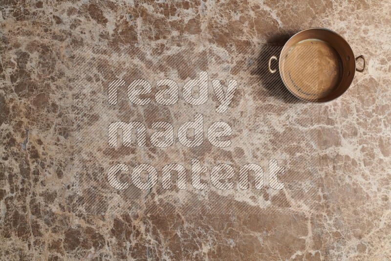 A small copper pan on beige marble background