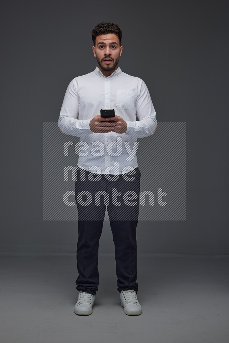 A man wearing smart casual standing and using his phone eye level on a gray background