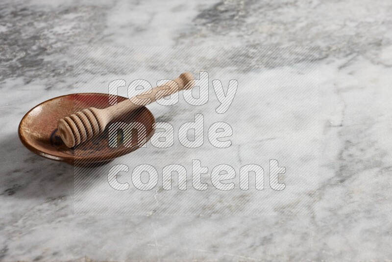 Decorative pottery plate with wooden honey dipper in it on grey marble background