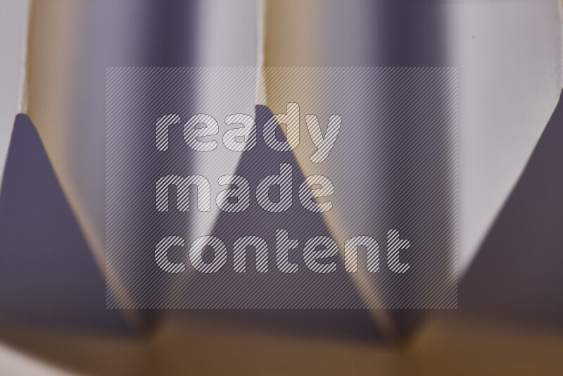 A close-up abstract image showing sharp geometric paper folds in white gradients and warm tones