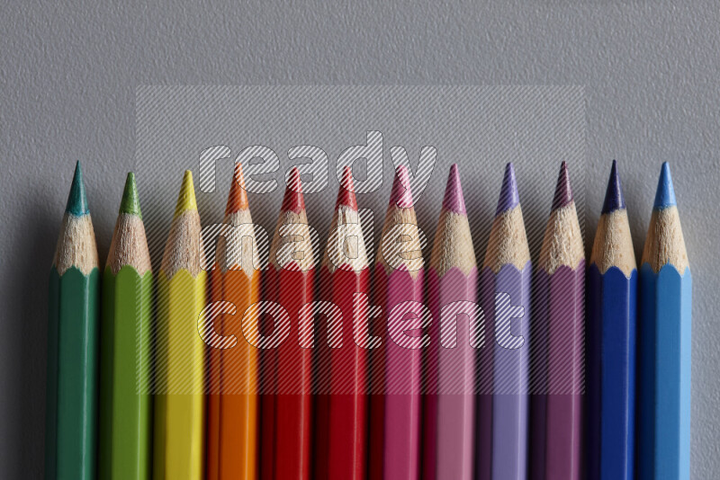 A collection of colored pencils arranged showcasing a gradient of different hues on grey background