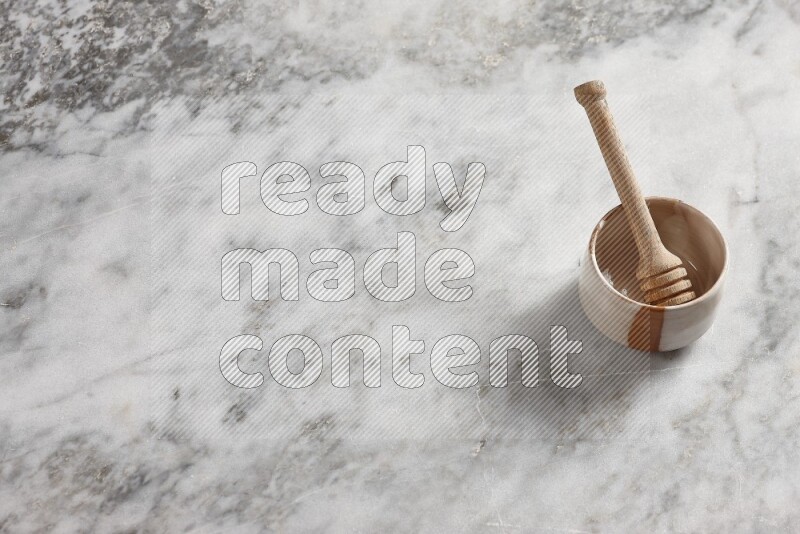 وعاء فخاري بيج مع ملعقة عسل خشبية بداخله على خلفية من الرخام الرمادي