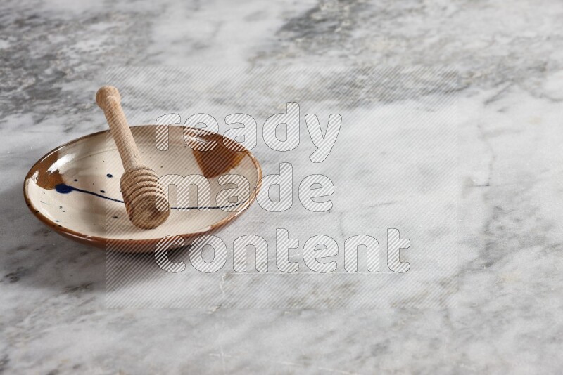Multicolored pottery plate with wooden honey dipper in it on grey marble background