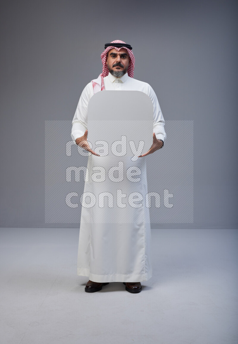 Saudi man Wearing Thob and red Shomag standing holding social media sign on Gray background