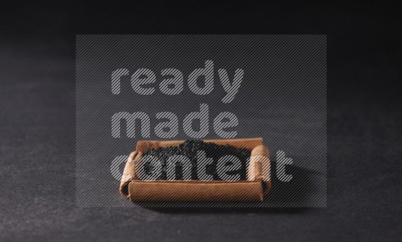 A single square of cinnamon sticks full of black seeds on black flooring