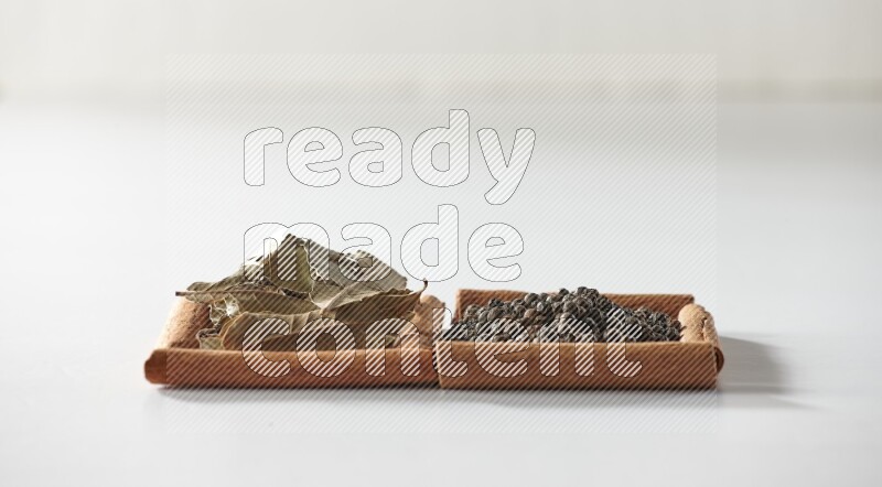 2 squares of cinnamon sticks full of black peppers and bay laurel leaves on white flooring