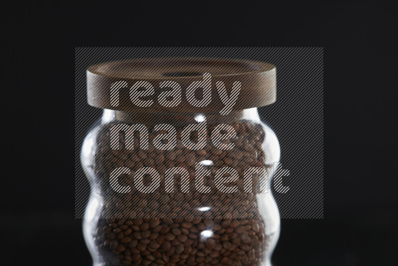Brown lentils in a glass jar on black background