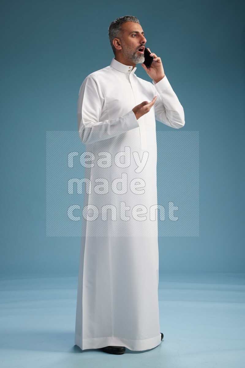Saudi man wearing thob talking on the phone on blue background
