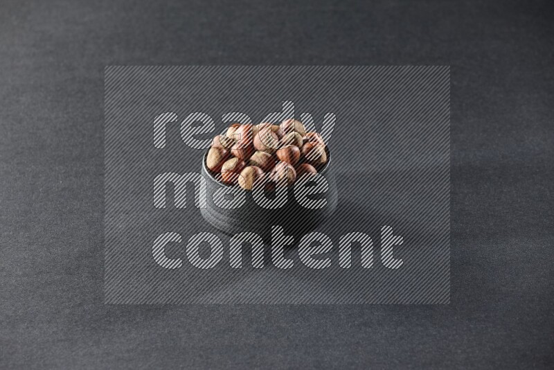 A black pottery bowl full of hazelnuts on a black background in different angles