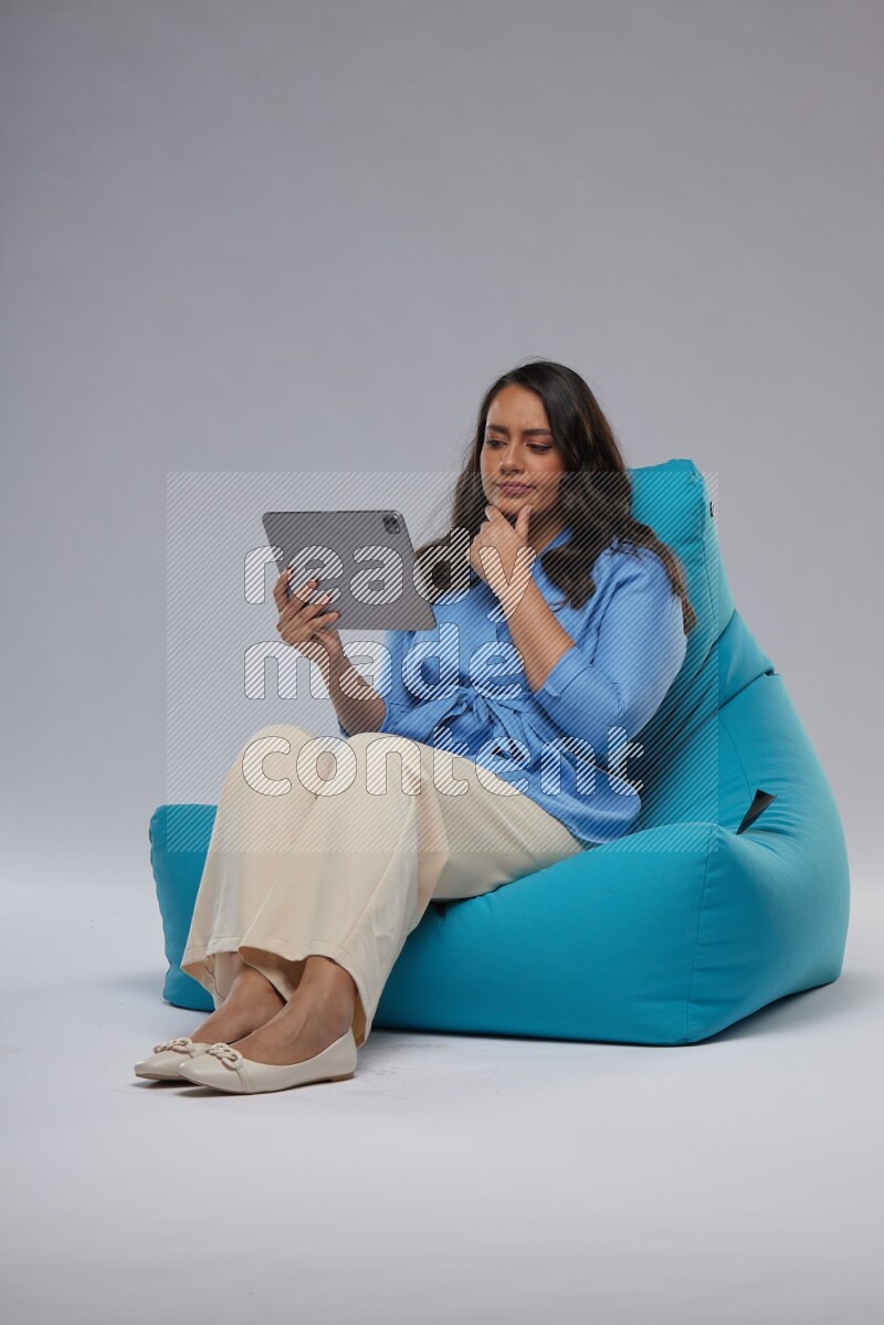 A woman sitting on a blue beanbag and working on tablet