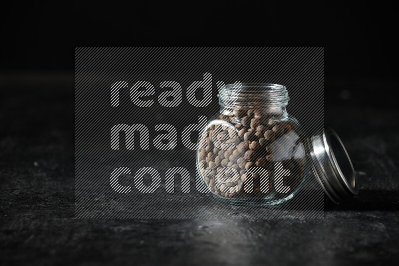 وعاء زجاجي للتوابل ممتلئ بحبوب بهار الفلفل الحلو منه على خلفية سوداء