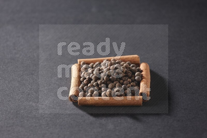 أربعة من أعواد القرفة مكونة شكل مربع بداخلها بهار الفلفل الحلو علي خلفية سوداء