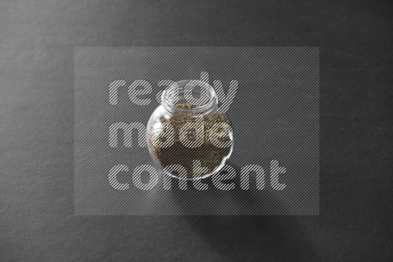 A glass spice jar full of cumin on black flooring