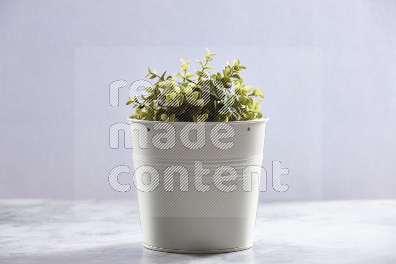 Green artificial plant in white pot on grey marble background