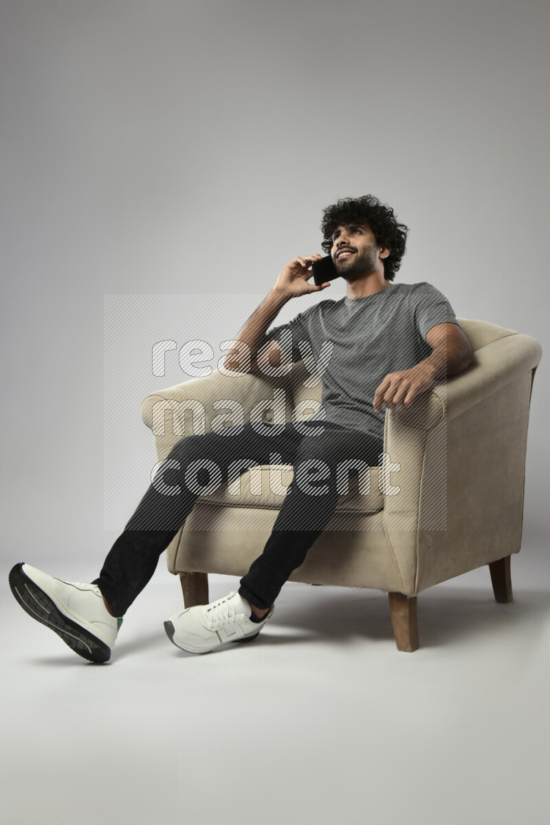 A man wearing casual sitting on a chair talking on the phone on white background