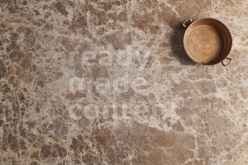 A small copper pan on beige marble background