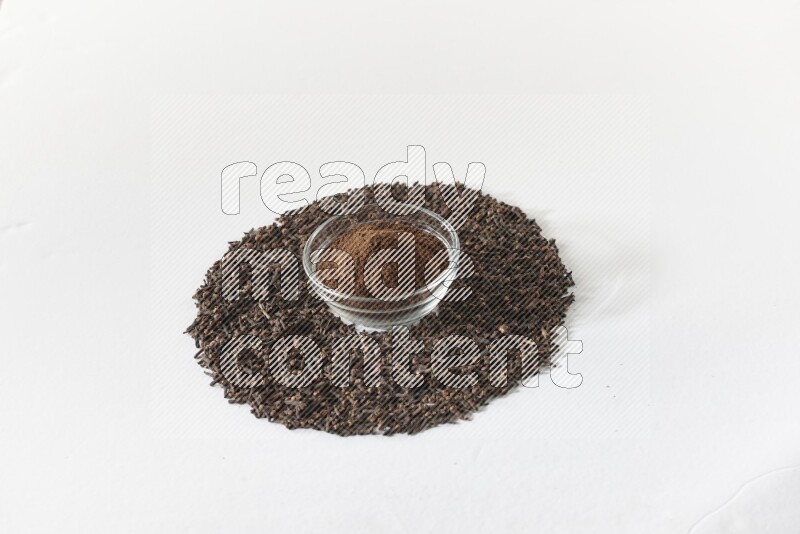 A glass bowl full of cloves powder and cloves grains spread on white flooring