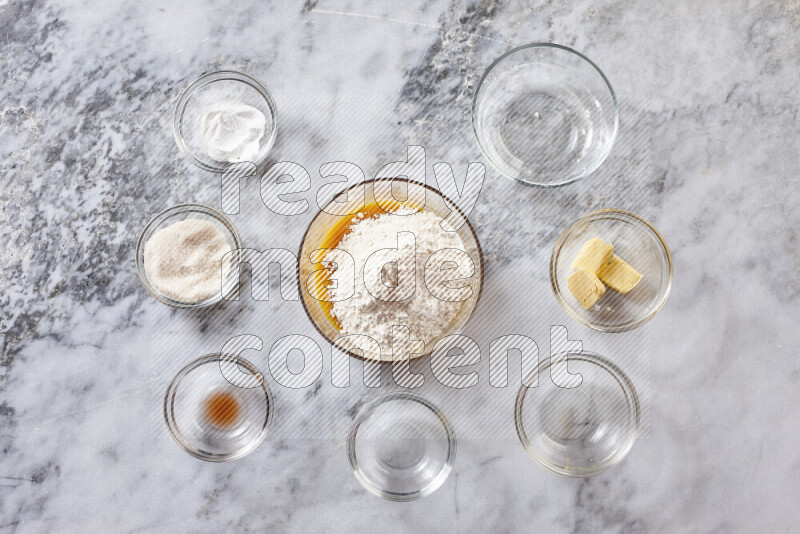 كوكيز خطوة بخطوة بمكوناتها، الدقيق، الزبدة، السكر البني، البيض، الفانيليا، السكر الأبيض، رقائق الشوكولاتة وصودا الخبز على خلفية رخام رمادي