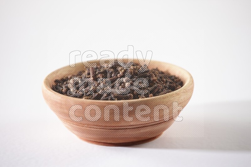 A wooden bowl full of cloves on a white flooring