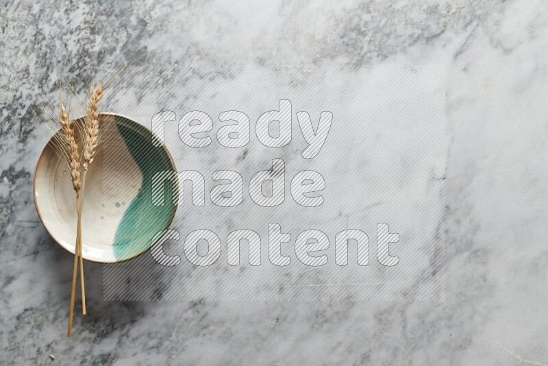 Wheat stalks on multicolored pottery plate on grey marble background