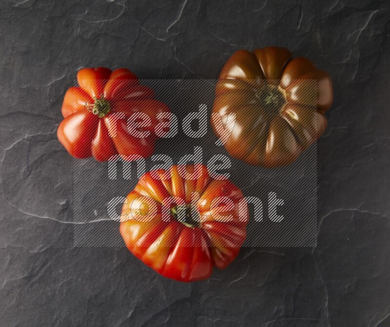 three heirloom tomatoes topview on a black slate background