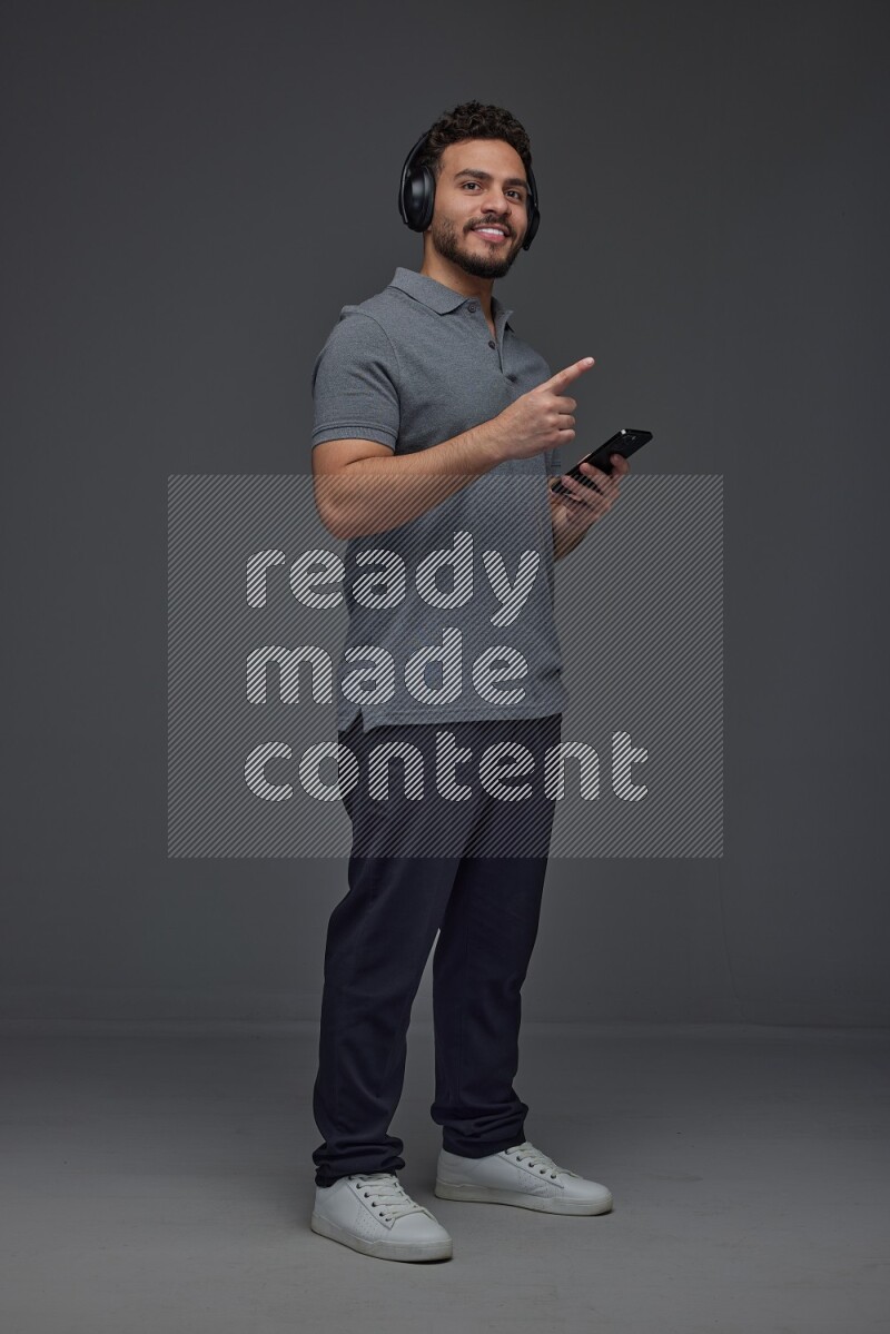 A man wearing casual and using his phone and headphone eye level on a gray background