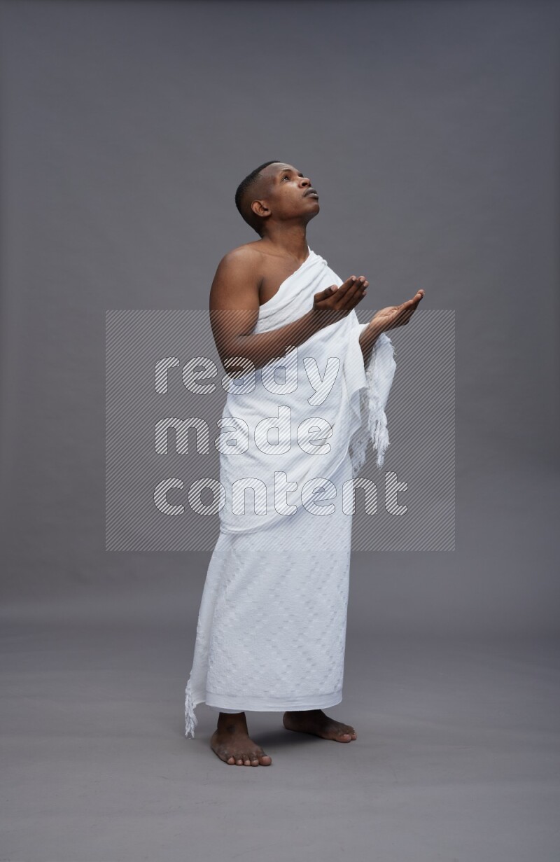 A man wearing Ehram Standing dua'a on gray background