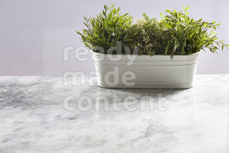 Multiple green artificial plants in white pot on grey marble background