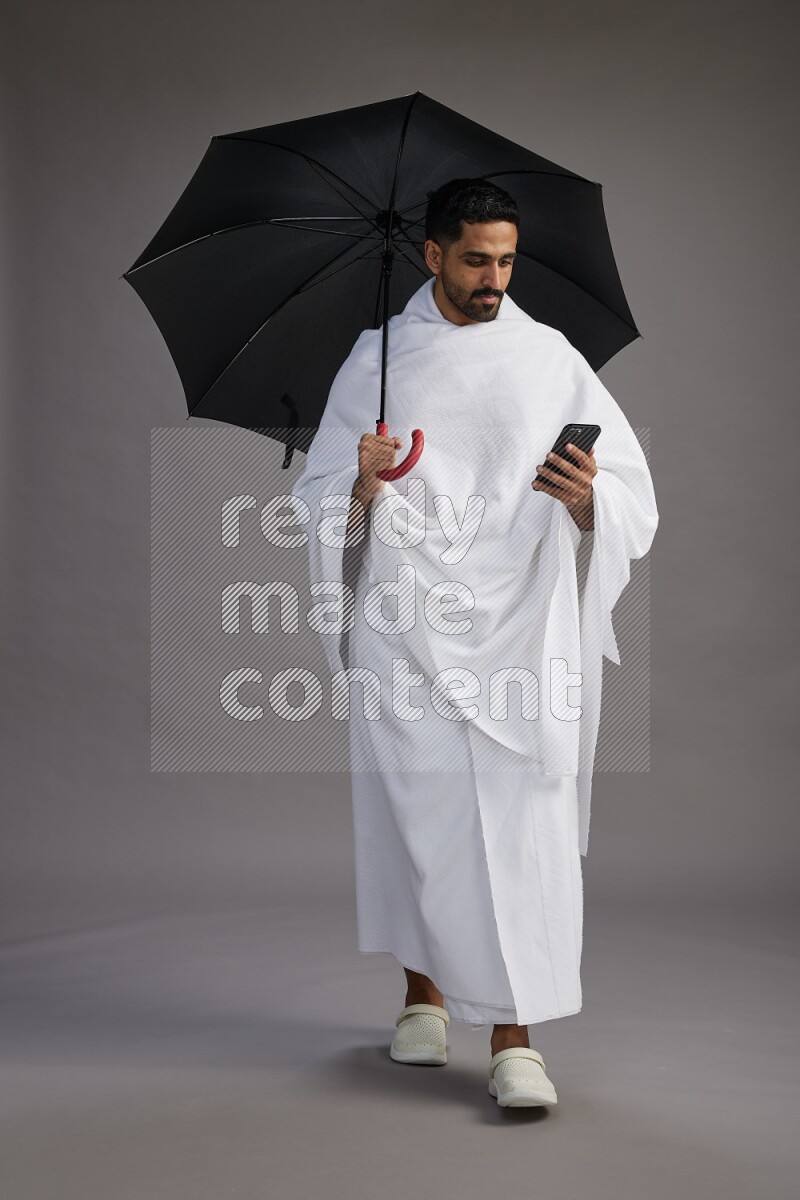 A man wearing Ehram Standing holding umbrella on gray background