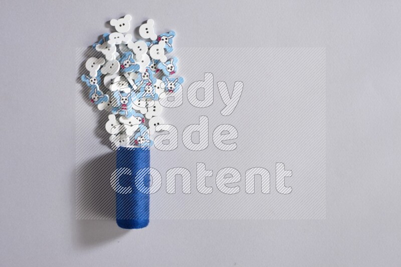 A blue sewing thread spool with colored buttons on grey background