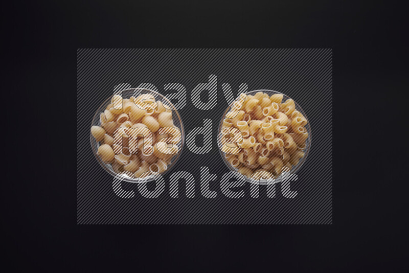 Different pasta types in glass bowls on black background