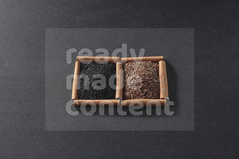 2 squares of cinnamon sticks full of flaxseeds and black seeds on black flooring