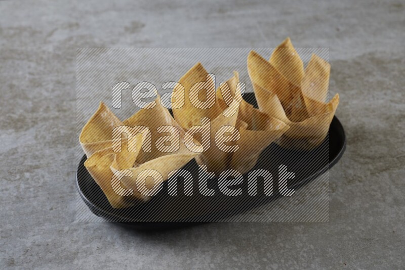 wonton cups on oval black ceramic plate on grey textured counter top