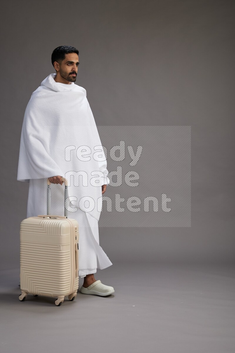 A man wearing Ehram Standing holding traveling bag on gray background