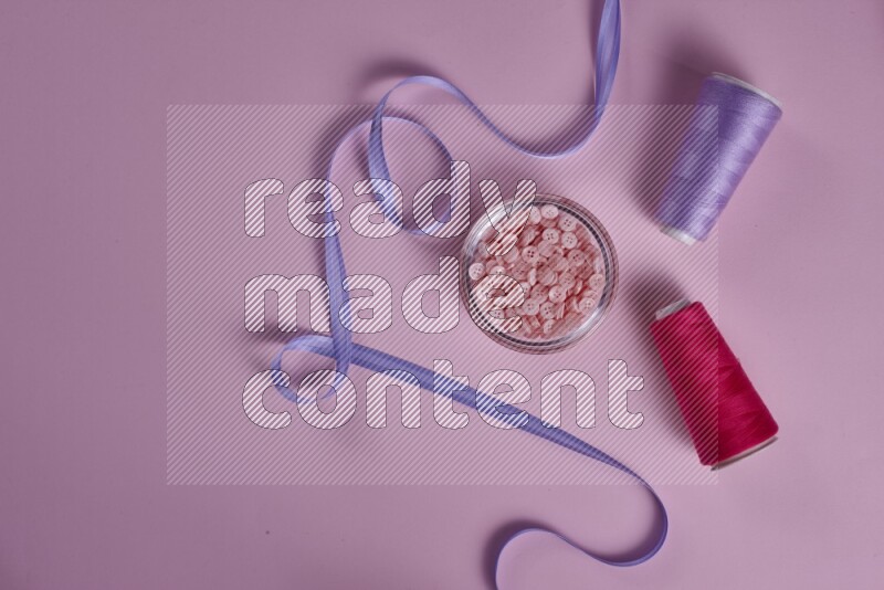 مجموعة من أدوات الخياطة والتفصيل أرجوانية وزهرية اللون على خلفية زهرية