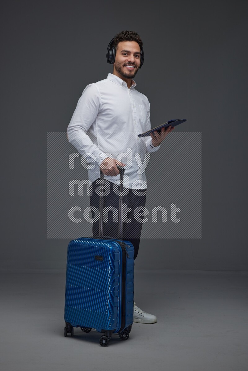A man wearing smart casual with and pulling a carry-on luggage eye level on a gray background