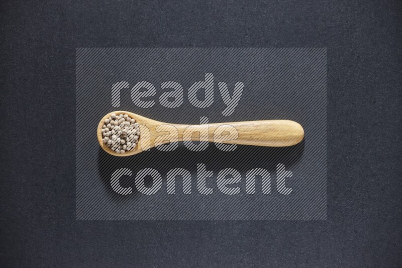 A wooden spoon full of white pepper beads on black flooring