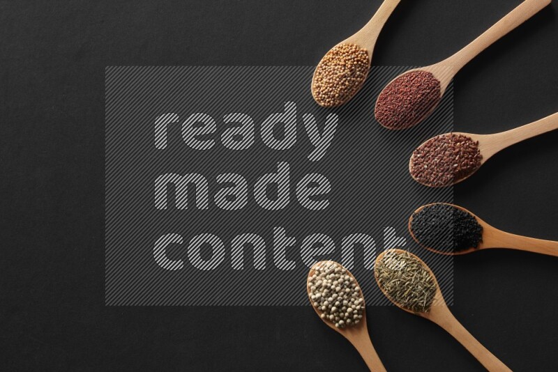 الفلفل الأسود وحبوب الخردل وحبة البركة وحب الرشاد والكمون و حبوب الكتان في معالق خشبية علي خلفية سوداء