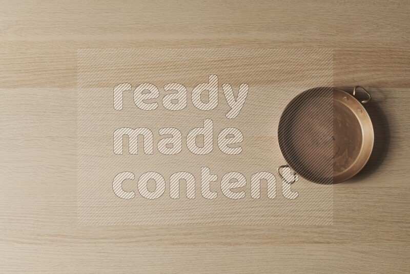 مقلاة نحاسية صغيرة على خلفية خشبية فاتحة