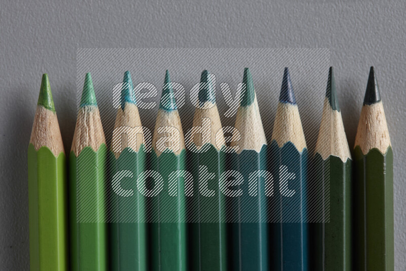مجموعة من أقلام الرصاص الملونة مرتبة لتعرض تدرجا من الألوان الخضراء علي خلفية رمادية