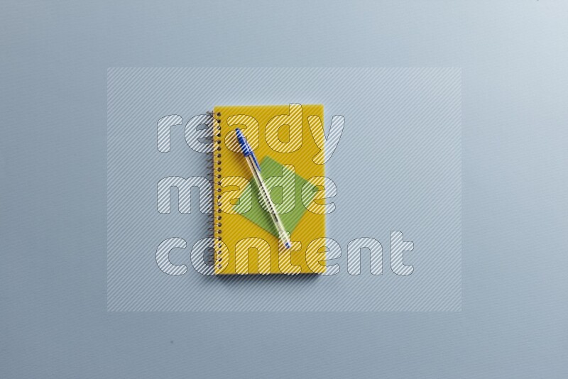 A yellow notebook with different school supplies on blue background