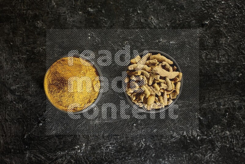 وعاءان من الفخار باللون الأسود، أحدهما ممتلئ ببودرة الكركم والآخر ممتلئ بأصابع كاملة من الكركم المجفف على خلفية سوداء