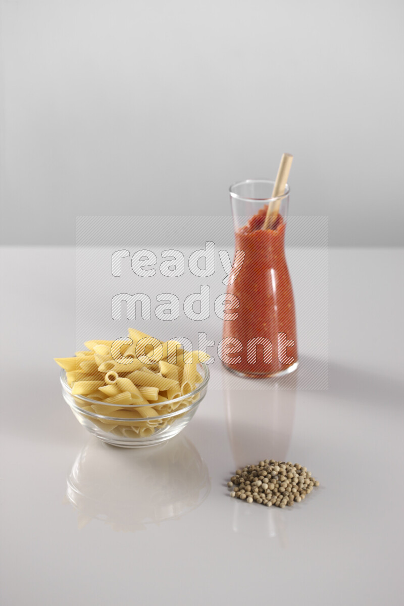Raw pasta with tomatoe pasta with different ingredients such as cherry tomatoes, basil, garlic, bay laurel, cardamom, white pepper, black pepper, red chilis and wheat stalks on light grey background