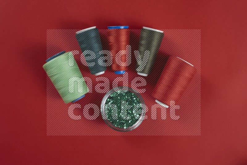 A green and red collection of sewing and tailoring tools arranged on a red background