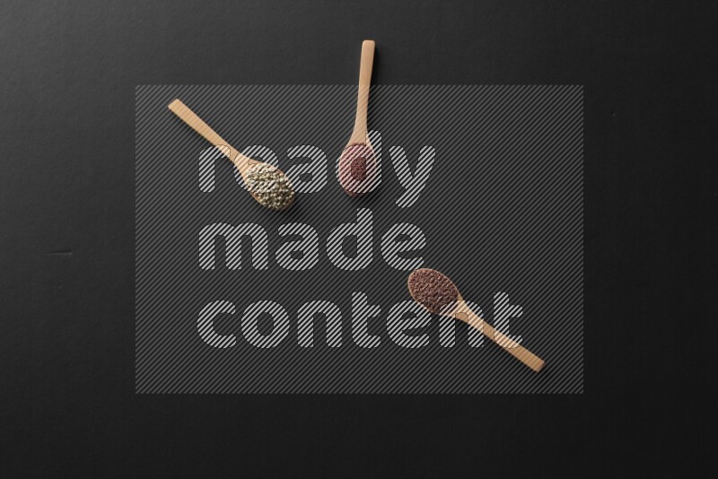 wooden spoons filled with white peppers, mustard seeds, black seeds, garden cress, cumin and flax on black flooring