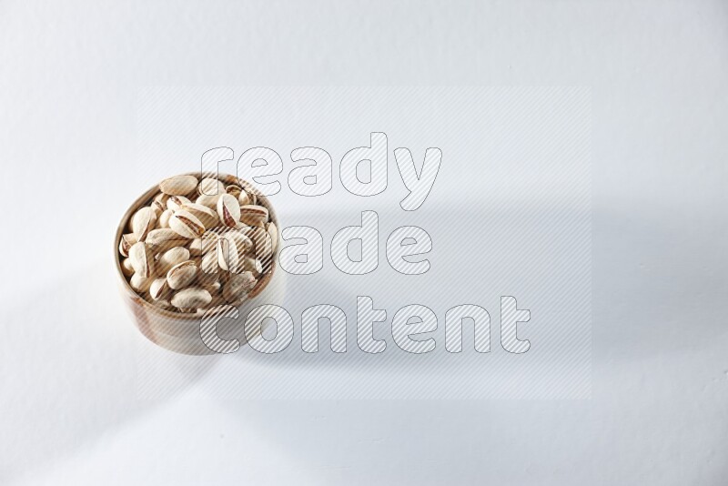 A beige ceramic bowl full of pistachios on a white background in different angles