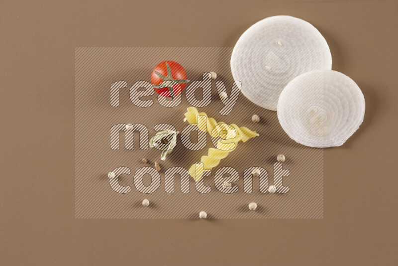 Raw pasta with different ingredients such as cherry tomatoes, garlic, onions, red chilis, black pepper, white pepper, bay laurel leaves, rosemary and cardamom on beige background