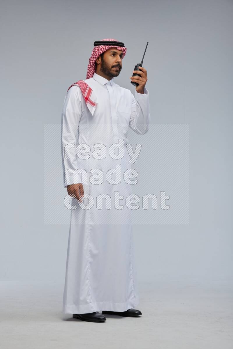 Saudi man Wearing Thob and shomag standing holding walkie-talkie on Gray background
