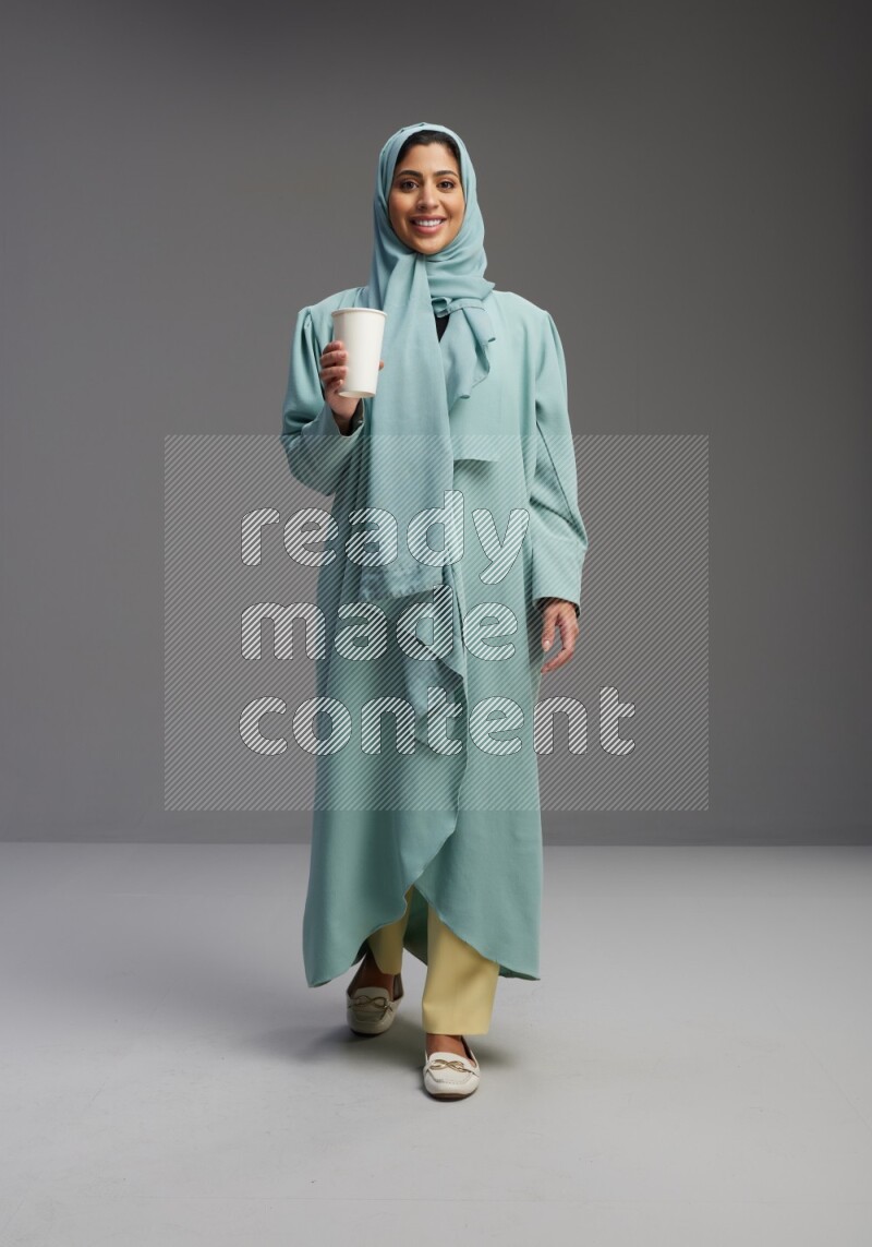 Saudi Woman wearing Abaya standing  holding paper cup on Gray background